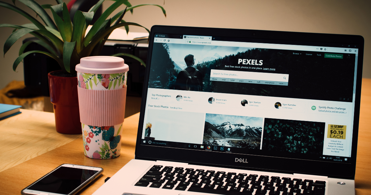 Notebook sobre uma mesa com planta e xícara de café, exibindo um site de fotos e conteúdo visual
